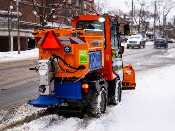 Orange sidewalk plow dispersing salt