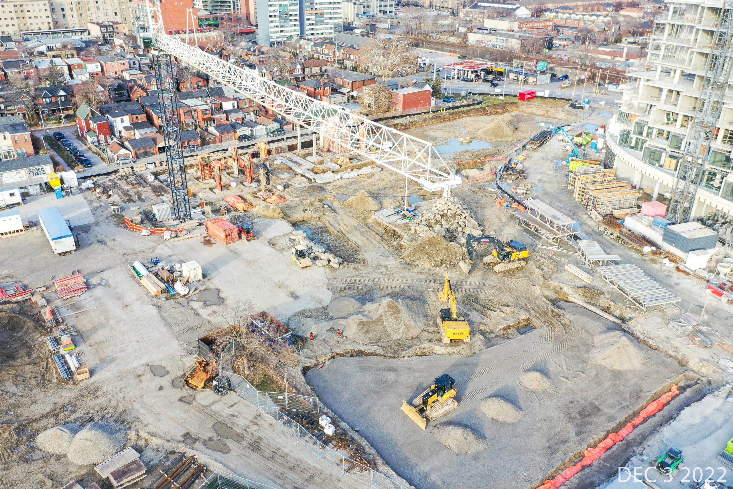 An aerial photograph of the construction site at Wallace Emersion Community Centre on December 3, 2022, which shows a large crane and multiple excavators and construction equipment. The construction area is predominantly flat, with soil and sand throughout. 