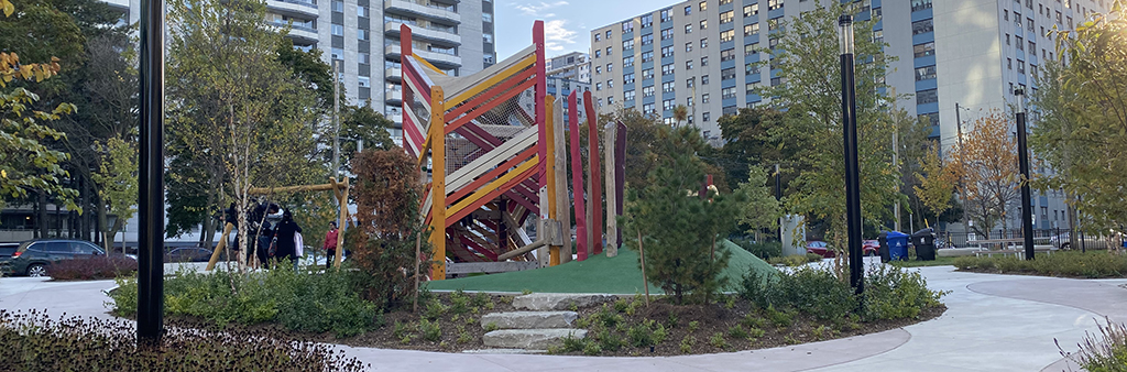 View of the new park at 60 Howard Street facing southwest, showing multiple paths and playground in the centre surrounded by plantings.