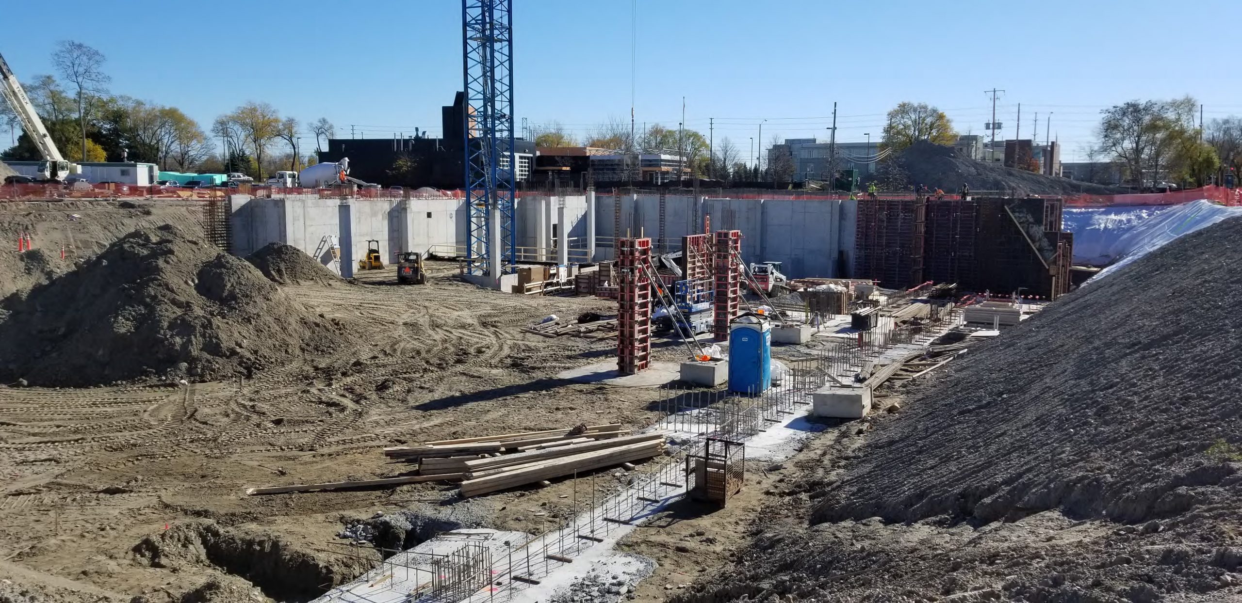 A photograph of the construction site at North East Scarborough Community Centre, which shows below-ground excavation work, including a partially complete concrete foundation wall, crane, and construction material. 