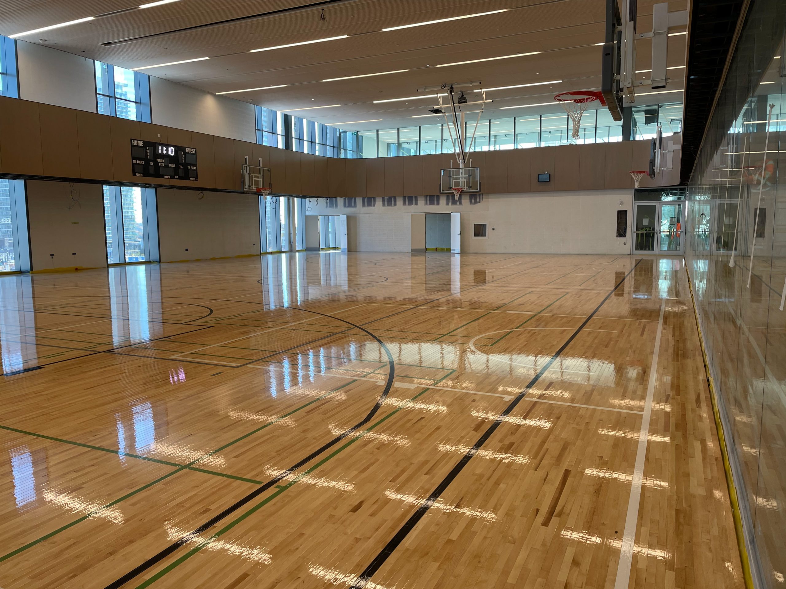 A photograph showing the construction progress of the gymnasium in the new Ethennonnhawahstihnen’ Community Recreation Centre. The photo shows a substantially completed gym, with basketball nets and a walking tracking on the second level around the perimeter of the gym. 