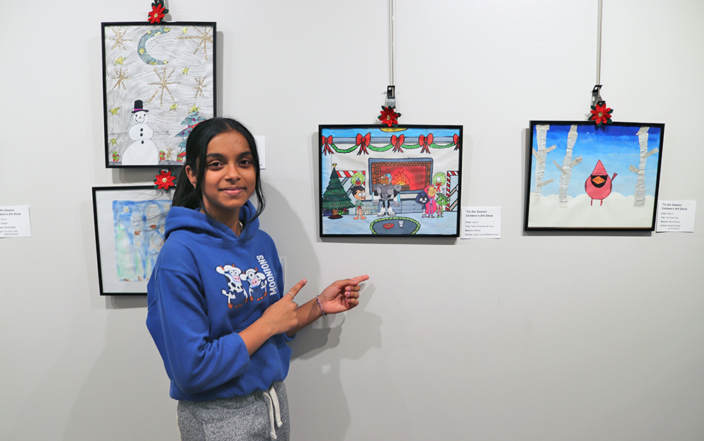 Photo of a student standing with their artwork in display in a gallery