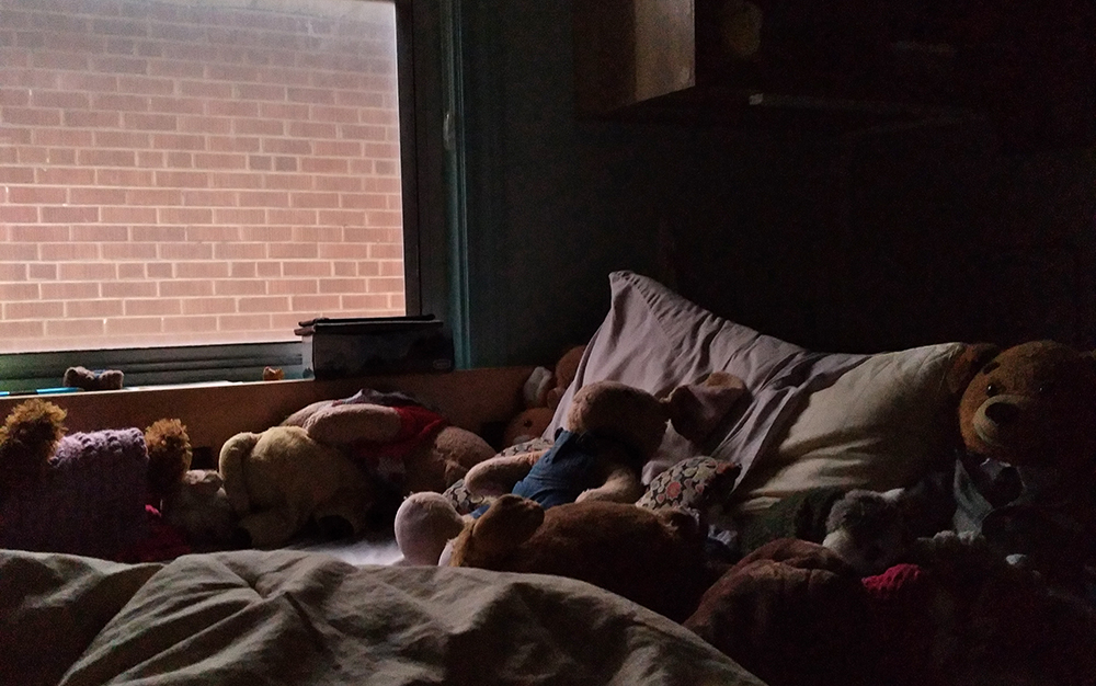 Photo of a dimly lit bed with teddy bears in front of a window