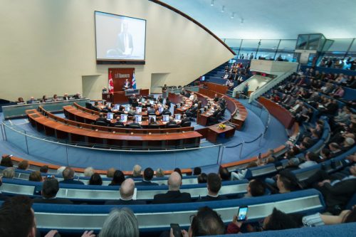 Large group of people seated in a semi-circular meeting room. 