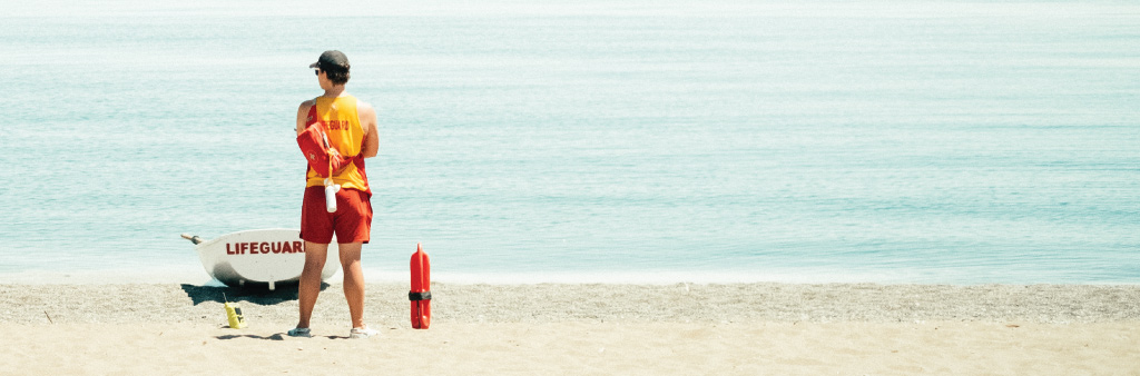 A lifeguard stands by their station on the beach, looking out towards the water.