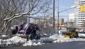 Small sidewalk snow plows clearing a snow covered sidewalk on a sunny winter day