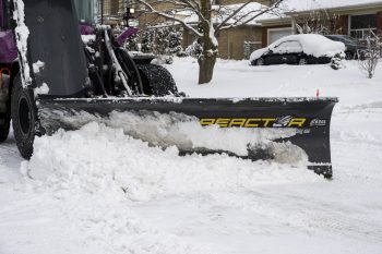 cropped view of a snow plow showing the front blade removing snow from a road on a winter day