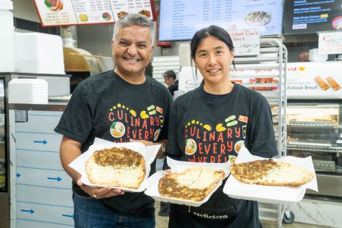 Two people smiling and holding restaurant food towards camera
