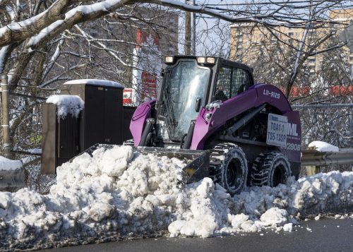 cropped view of a sidewalk snowplow removing snow on a residential sidewalk