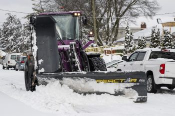a snow plow clearing snow from a road on a residential street