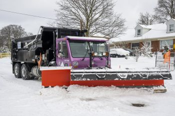 a large colourful snow plow clearing snow from a residential road