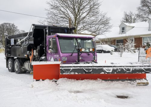 a large colourful snowplow clearing snow from a residential road