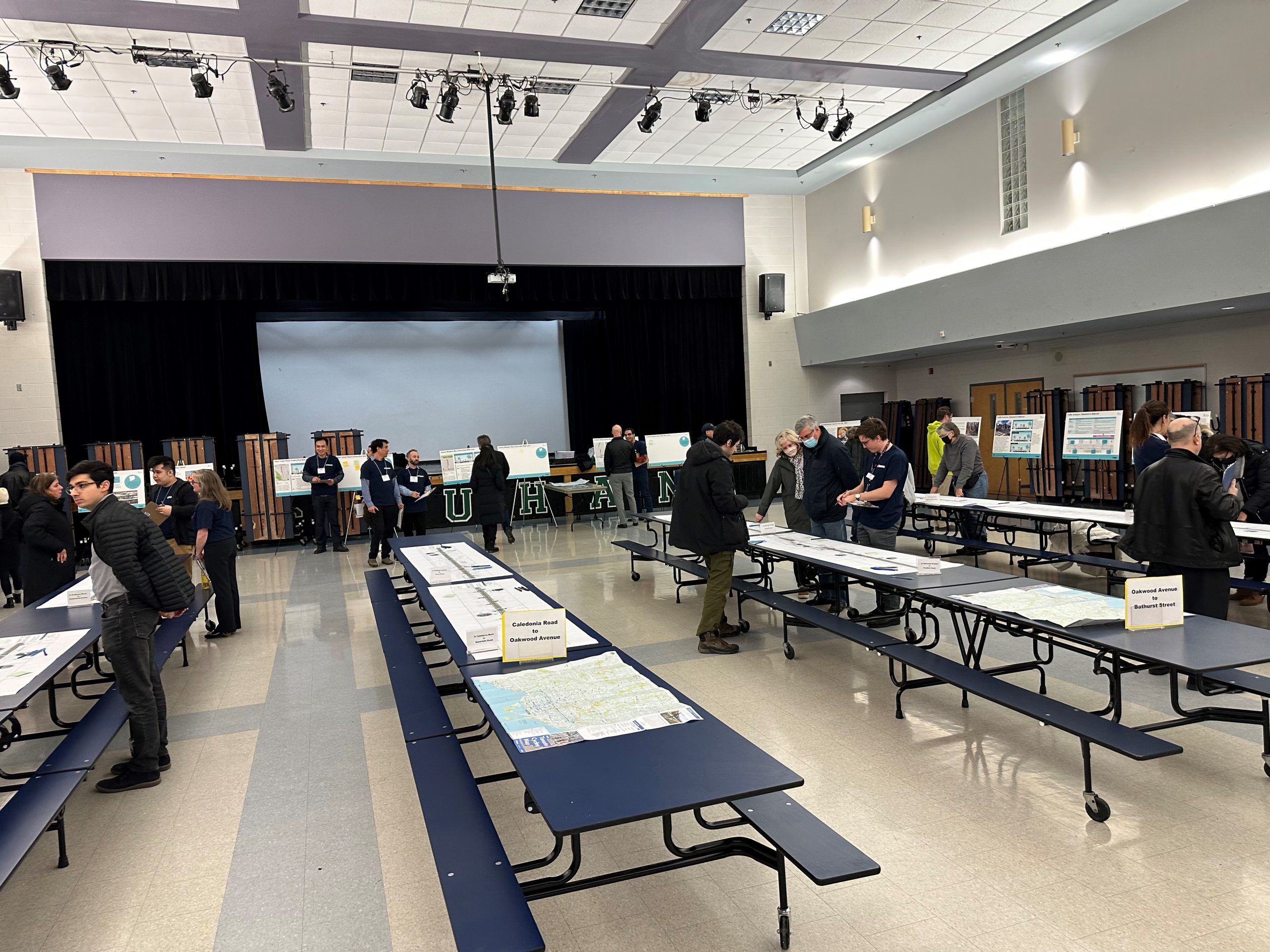 eglintonTOday drop-in event hosted at Marshall McLuhan Catholic Secondary School showing tables with design plans and people speaking with City staff.