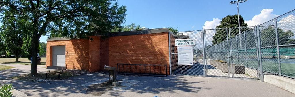 A photograph of the clubhouse in Clydesdale Park which shows a one storey brick building adjacent to the fenced tennis courts with mature trees in the background.