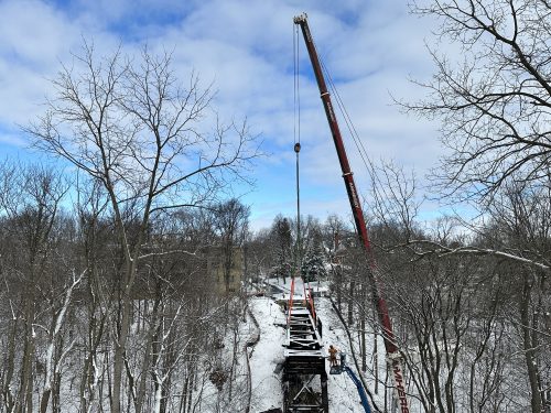 An overhead crane lifts pieces of the pedestrian bridge away.