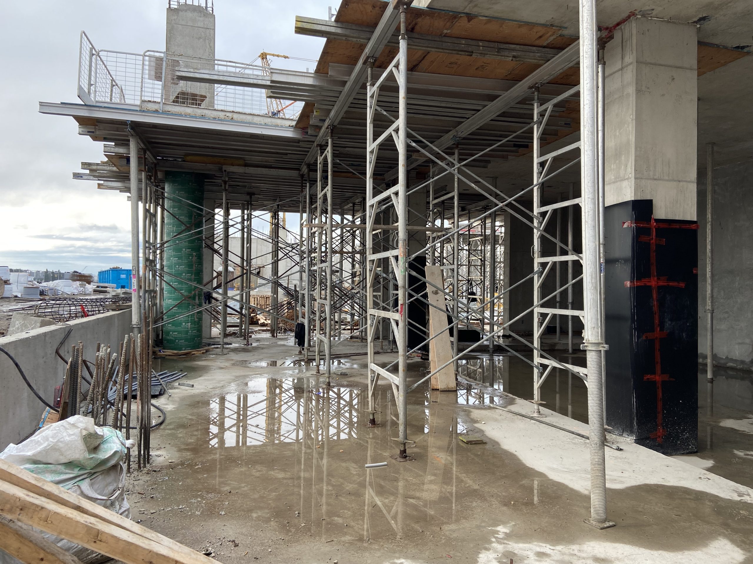 Photograph of the construction for the new East Bayfront Community Recreation Centre, looking south within the future main floor lobby area and dance studio on the right. The images show a construction site with steel scaffolding.