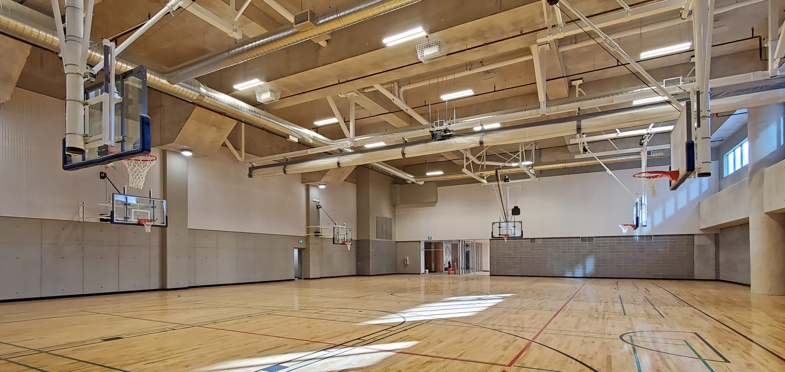 A photo of the indoor double-gymnasium at One Yonge Community Recreation Centre which shows a large gym with six basketball hoops and the unfinished gym entrance in the background.