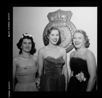 Photograph depicts three women wearing ball gowns