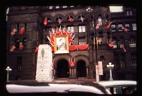 Photograph depicts Old City Hall decorated with oversize portait of Queen Elizabeth II, Union Flags and Canadian Red Ensigns