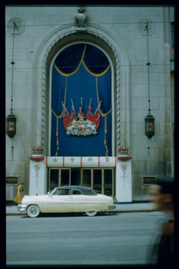 Photograph depicts store front decorated with Royal Coat of Arms, Union Flags and Canadian Red Ensigns