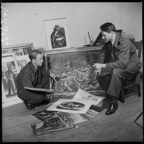 2 men in army uniforms holding paint brushes with paintings and sketches around them.