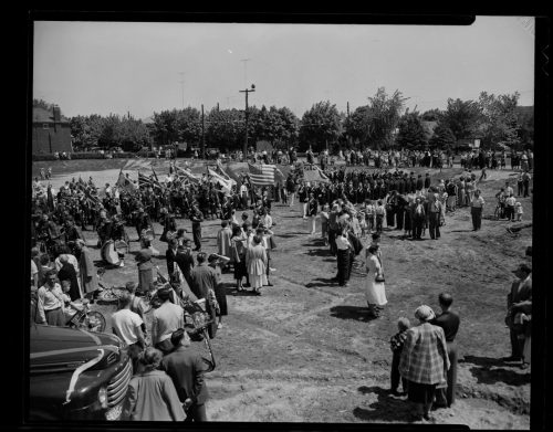 Image depicts crowd of people watching parade in park