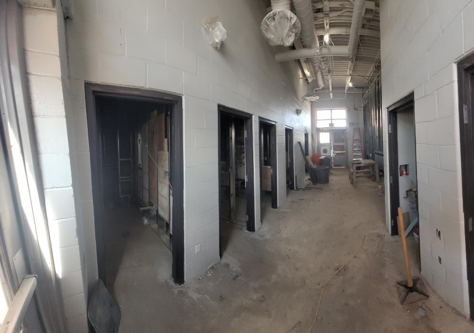 A photo of the interior of the Clubhouse in Dufferin Grove Park during construction which shows a hallway with doorways to seven different rooms. Construction equipment can be found throughout. 