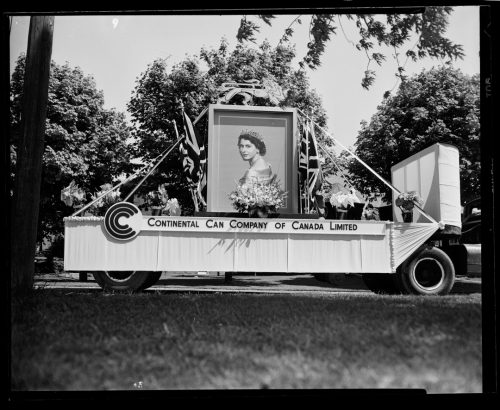 Image depicts wheeled float decorated with oversize portrait of Queen Elizabeth II and Union Flags
