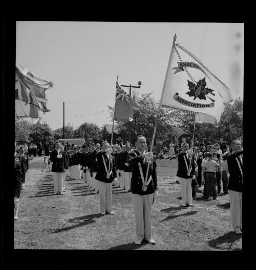 Photograph depicts men in parade carrying flags