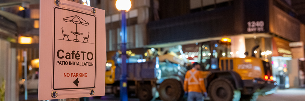 CafeTO sign indicates no parking as crews install traffic safety equipment to close the curb lane.