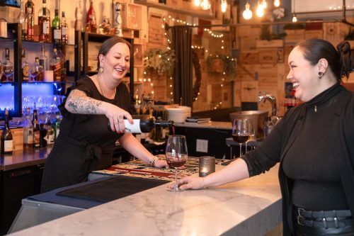 Smiling bartender pours a glass of red wine
