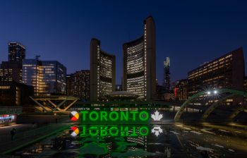Nathan Phillips Square Toronto Sign lit green at night, City hall in the background