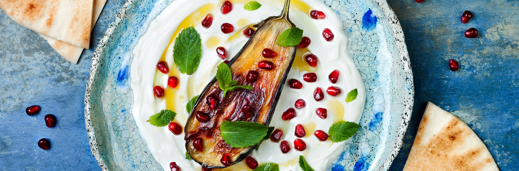 Eggplant meal with mint leaves and pomegranate seed on a sauce sitting on a plate and flatbread on the side