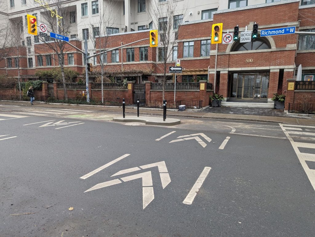 Concrete curb island located at the north side of Richmond Street West at Brant Street.