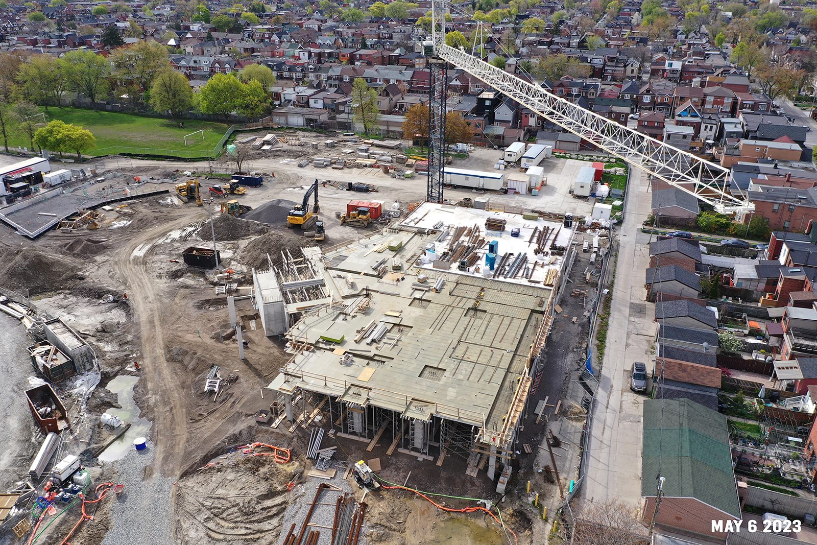 An aerial photograph of the construction site at Wallace Emersion Community Centre on May 6, 2023, which focuses on the community centre while under construction and a large crane over the site. The structure is one-storey with concrete columns, construction scaffolding and materials throughout. 