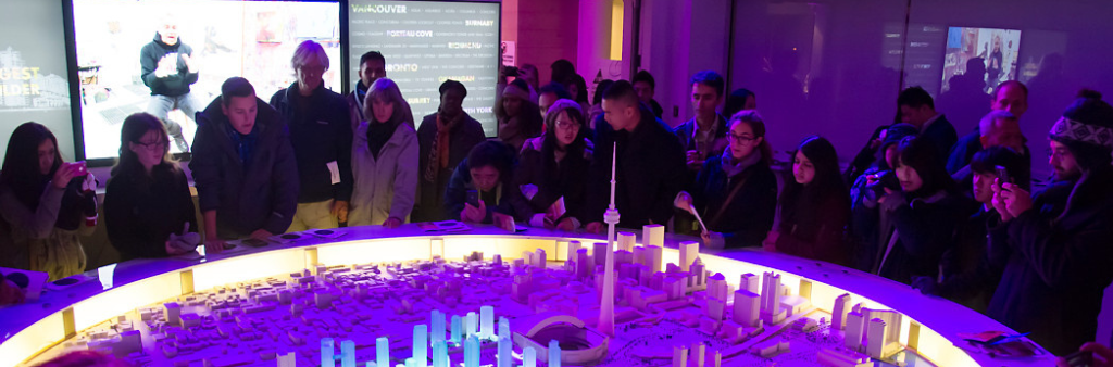 Crowd in a dark-lit room gathered around a lit 3D model of downtown Toronto