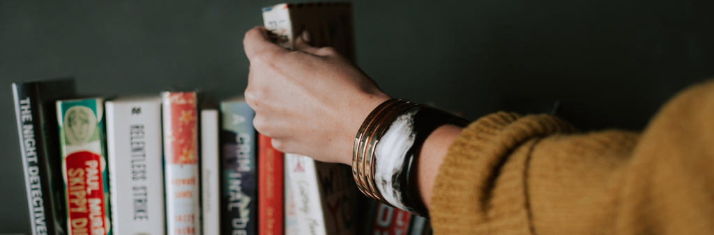 Close up of a arm reaching to pull book off a shelf of many books