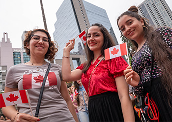 Three people dressed for Canada Day and holding Canadian flags.