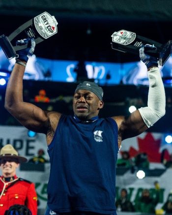 Henoc Muamba holding two Grey Cup trophies above his head. 