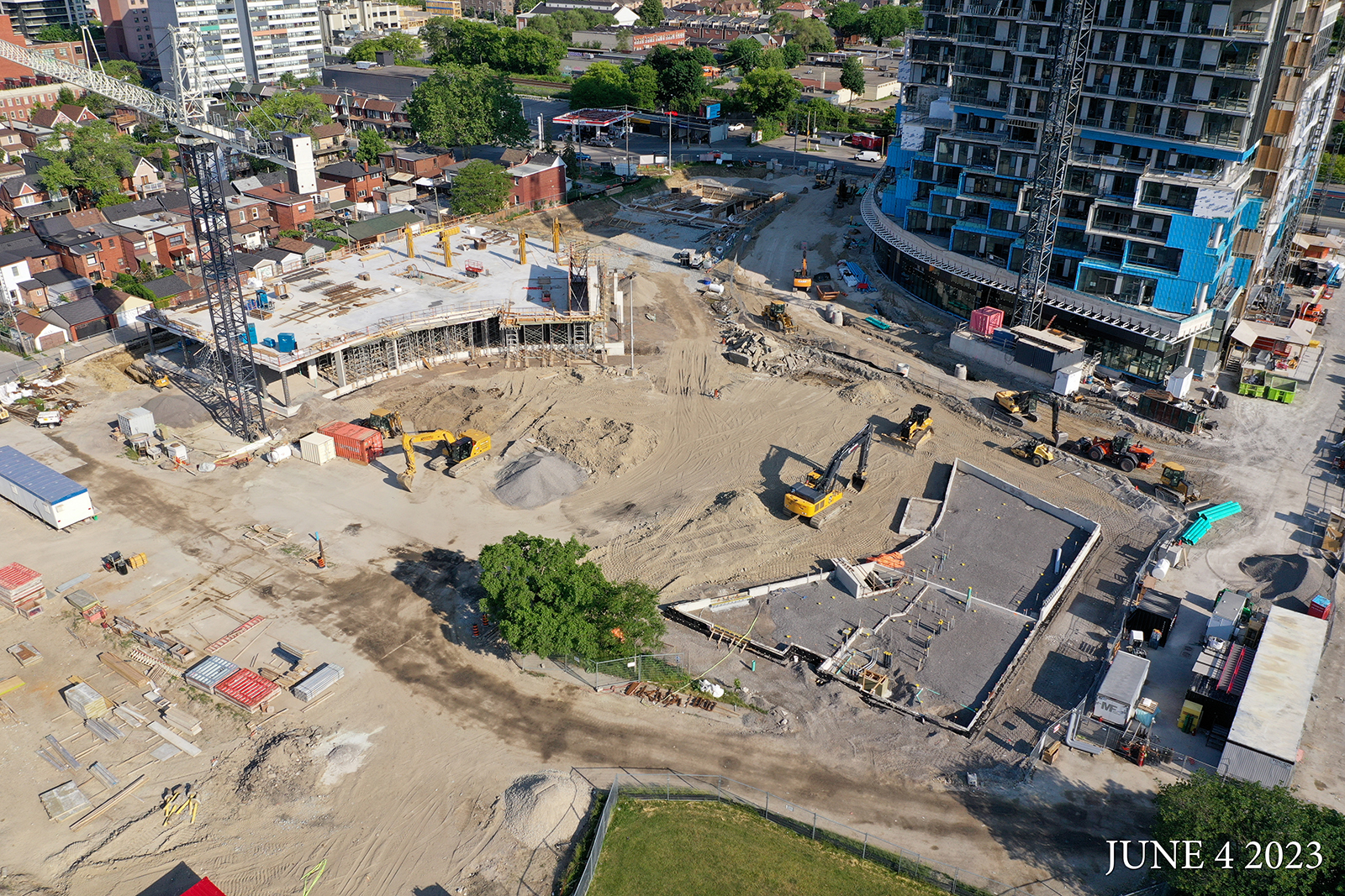 An aerial photograph of the construction site at Wallace Emersion Community Centre on June 4, 2023, which focuses on the community centre while under construction and the adjacent Fieldhouse. The community recreation structure is one-storey with concrete columns and a concrete slab and the Fieldhouse is at ground-level with a concrete slab. 