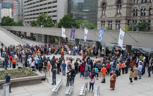 People standing in a circle around three fires in Nathan Phillips Square 