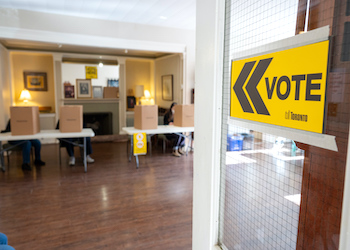 Toronto Elections yellow sign on a door reading vote with voting polls in a room.