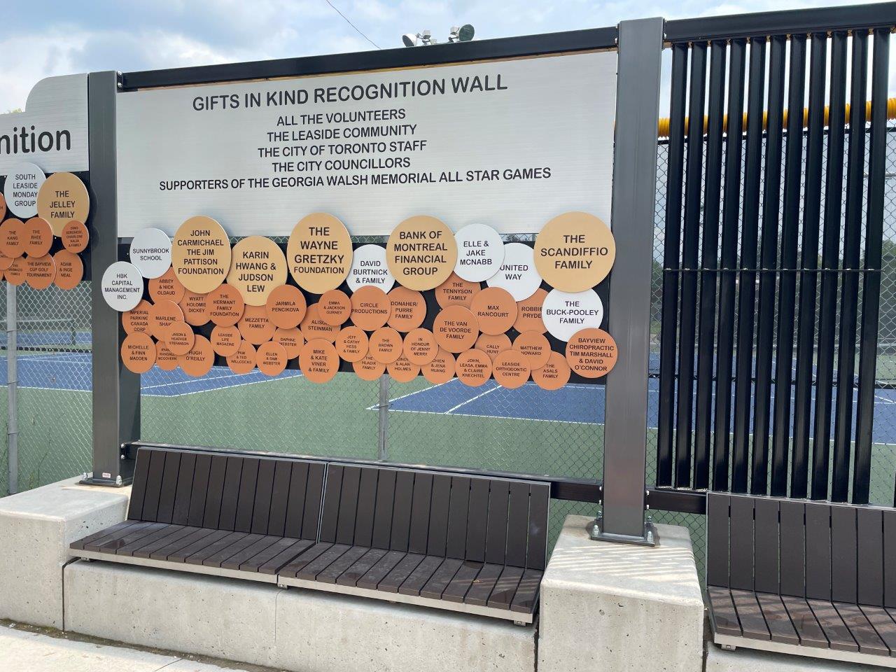 The Donor Wall shown along the exterior fence of the tennis courts with a bench below showing circular balloon shapes in different sizes and colours with donor names on each balloon.