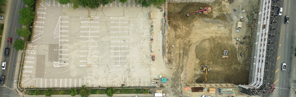 An aerial photo taken by drone showing 20 Castlefield Avenue, which is show as a flat concrete parking lot. To the right of the parking lot is a construction site, which is the development adjacent to Yonge Street. The future park site is located at the corner of Castlefield Avenue and Duplex Avenue.