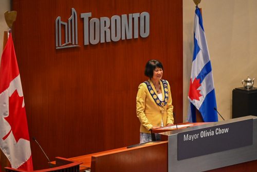Mayor Olivia Chow wearing a bright yellow blazer wearing a modern Chain of Office is composed of several elements joined together with pieces of chain with a medallion hanging from it. Toronto’s Chain of Office contains elements from all of the municipalities which were amalgamated into the present-day city of Toronto.