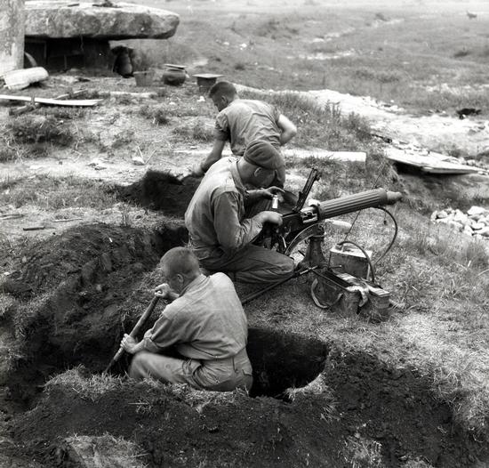 Three soldiers in the image; two are digging a trench, and the other is setting up a machine gun.