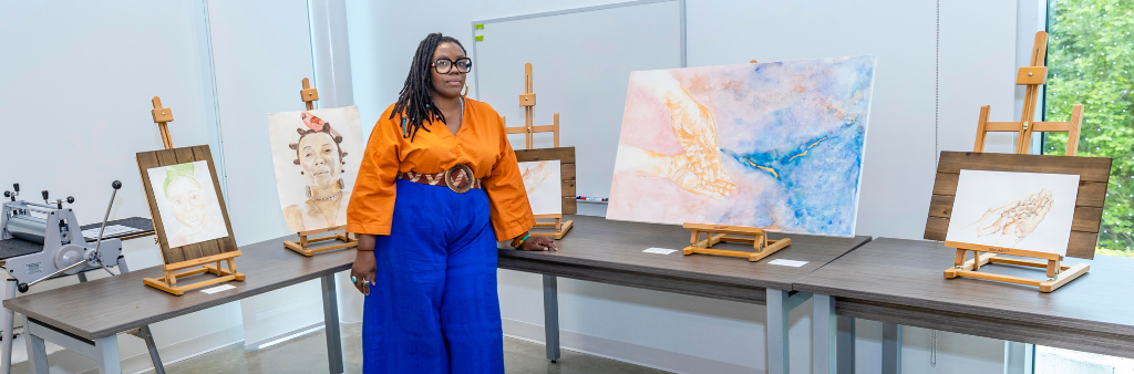 Person stands in front of two tables displaying artworks