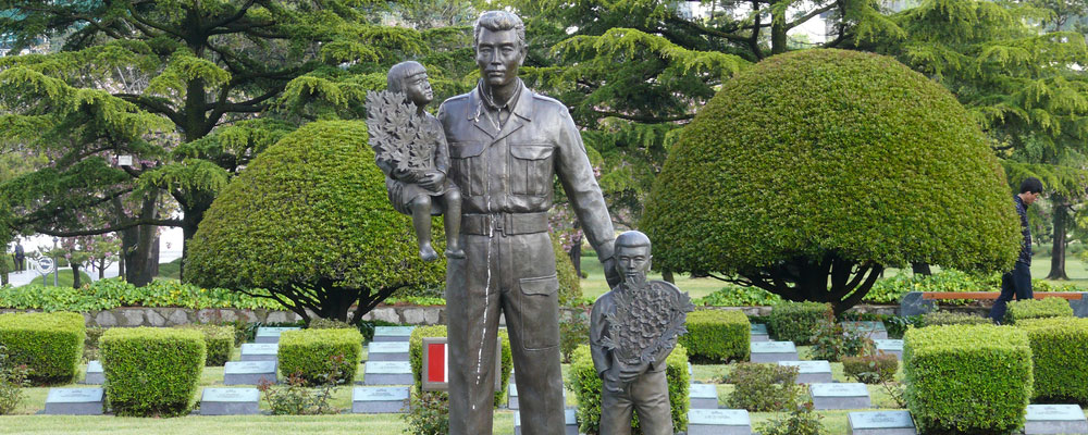 A statue in the United Nations Memorial Cemetery in Busan, South Korea, honouring the Canadian Fallen. The statue is a large bronze cast of a soldier, holding a young Korean girl, and on the other side, with a hand on the back of a young Korean boy.