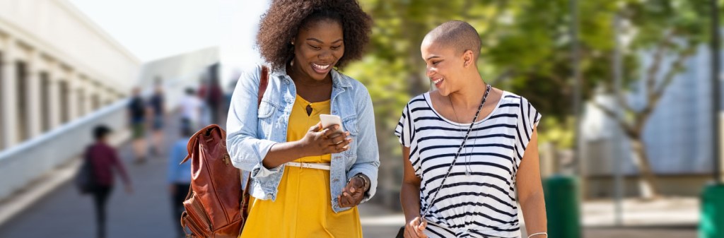 Two women walking together and looking at a mobile phone