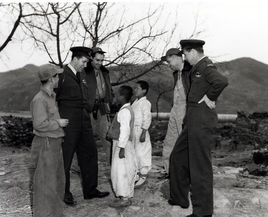 5 airmen are speaking with two young Korean children.